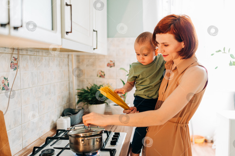 Скачать Счастливая мама со своим ребенком готовит на кухне. Уютный дом и рутинные обязанности фотосток Ozero