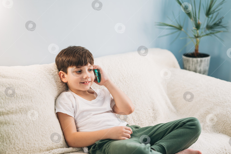 Скачать Ребенок разговаривает по смартфону, ребенок пользуется смартфоном, мальчик разговаривает в помещении фотосток Ozero