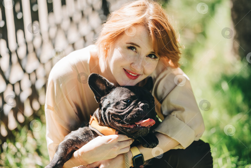 Скачать Щенок черного французского бульдога обнимается с девушкой-хозяйкой, лежащей на лужайке в парке на открытом воздухе летним весенним днем, целующейся, обнимающейся, ласкающейся. Счастливая женщина с собакой на улице фотосток Ozero