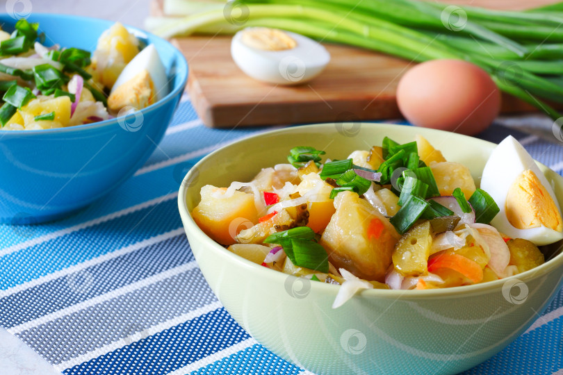 Скачать Картофельный салат в зеленых и синих мисках. на фоне разделочной доски - вареное яйцо и зеленый лук. фотосток Ozero