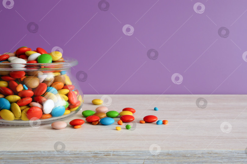 Скачать Разноцветные конфеты. Круглые конфеты в стеклянной банке на белом столе. Сиреневый фон фотосток Ozero
