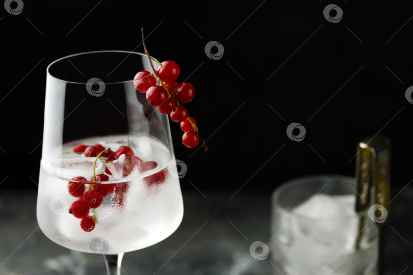 Скачать Очень крупный план бокала для вина с водой из красной смородины со льдом. Свежий фруктовый коктейль со льдом в бокале, освежающий летний напиток из ягод красной смородины на темном фоне, вид спереди. Напиток из красной смородины фотосток Ozero