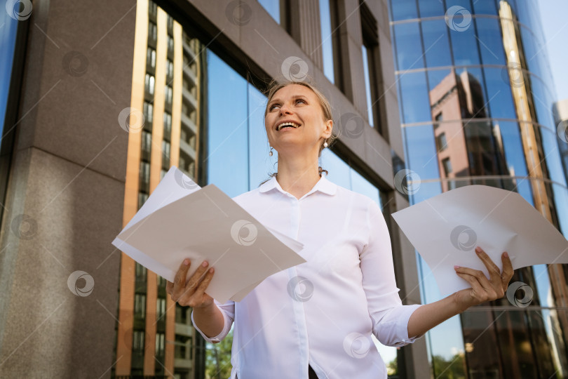 Скачать Деловая женщина с бумагами в руках на фоне офисного центра фотосток Ozero