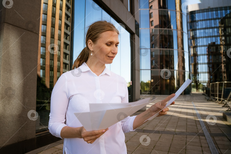 Скачать Деловая женщина с бумагами в руках на фоне офисного центра фотосток Ozero