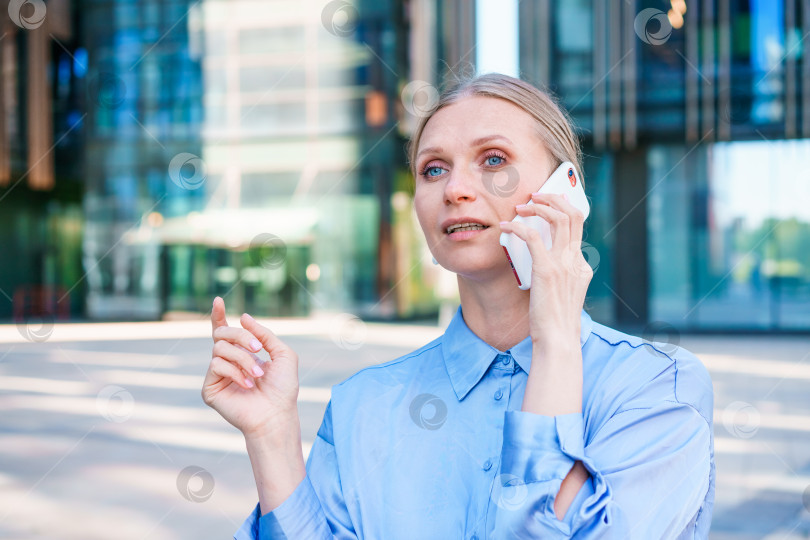 Скачать Успешная женщина-банкир пользуется смартфоном на открытом воздухе, стоя возле офиса фотосток Ozero