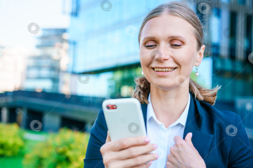 Скачать Успешная женщина-банкир пользуется смартфоном на открытом воздухе, стоя возле офиса фотосток Ozero