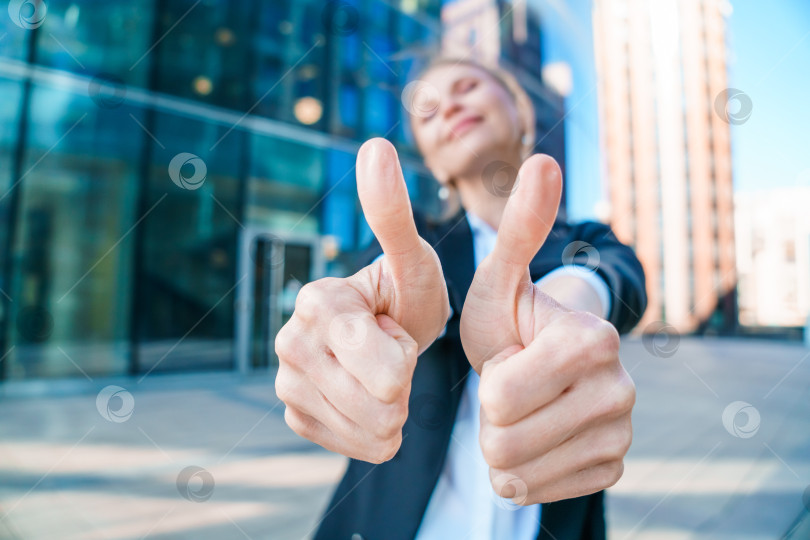Скачать Счастливая деловая женщина показывает большие пальцы вверх, стоя на открытом воздухе напротив офиса фотосток Ozero