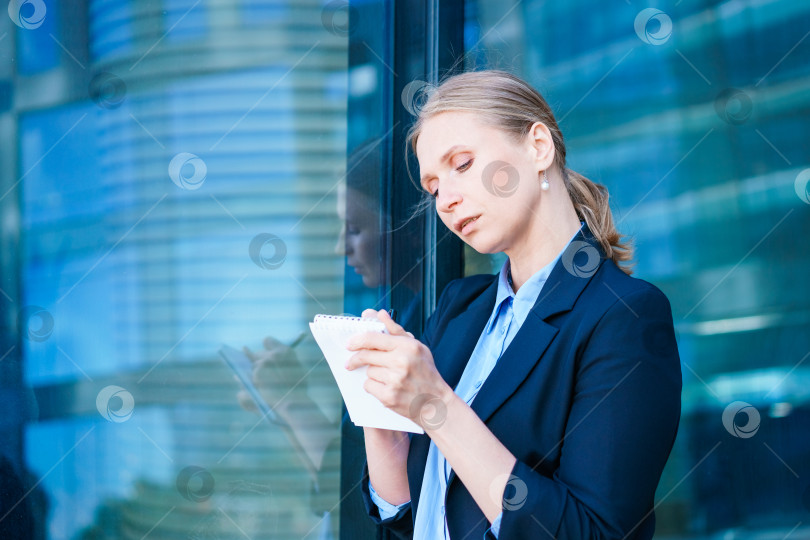 Скачать Успешная деловая женщина, делающая пометки в блокноте на открытом воздухе в деловой обстановке фотосток Ozero