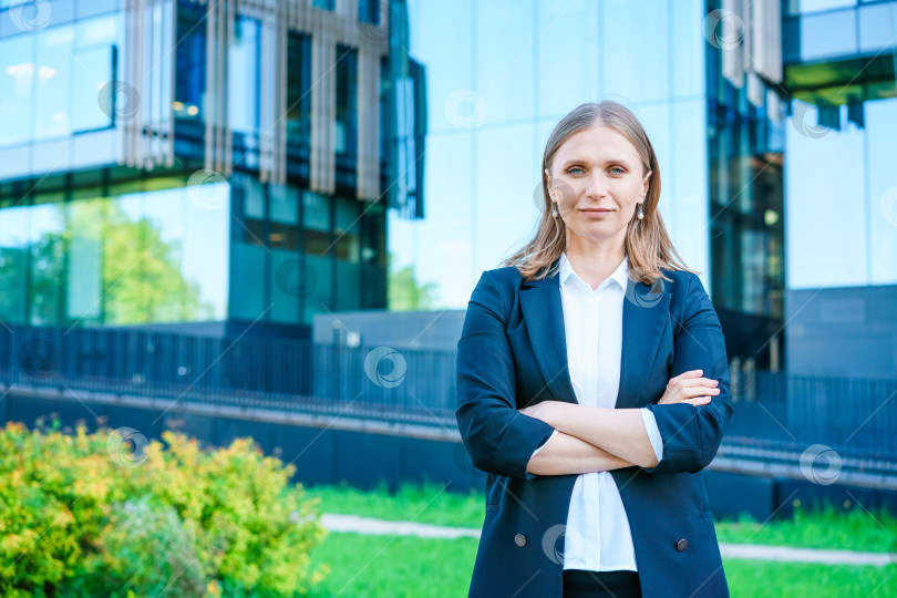 Скачать Успешная деловая женщина улыбается, счастливая, скрестив руки на груди, в городе на фоне фотосток Ozero