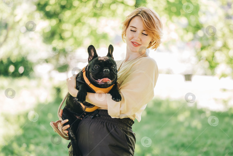 Скачать Щенок черного французского бульдога, обнимающийся с хозяйкой девочкой, лежащий на лужайке в парке на открытом воздухе летним весенним днем, целующийся, обнимающий, ласкающий. Счастливая женщина с собакой на улице фотосток Ozero
