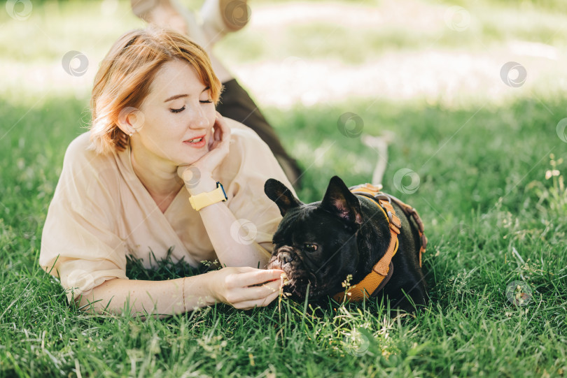 Скачать Щенок черного французского бульдога, прижимающийся к хозяйке, лежит на лужайке в парке на открытом воздухе летним весенним днем, целуется, обнимается, ласкается. Счастливая женщина с собакой на улице фотосток Ozero