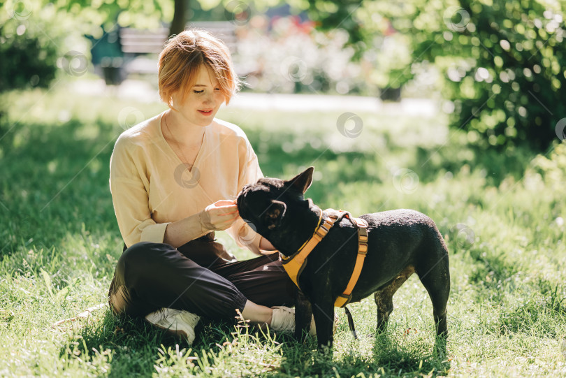Скачать Щенок черного французского бульдога обнимается с девушкой-владельцем, лежащей на лужайке в парке на открытом воздухе летом весенним днем, целующейся, обнимающейся, ласкающей. Счастливая женщина с собакой на улице фотосток Ozero