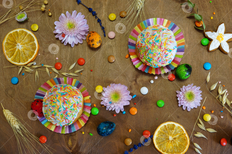 Скачать Куличи, цветные яйца, конфеты, цветы на деревянном столе. Вид сверху фотосток Ozero