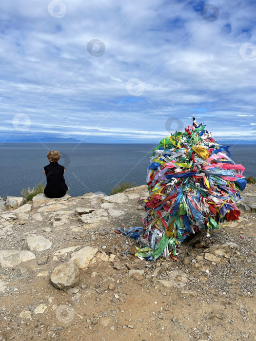 Скачать 20 июля 2022 года - Ольхон, Россия: Молодая девушка сидит на крутом утесе, глядя вдаль на мыс Хобой, озеро Байкал фотосток Ozero