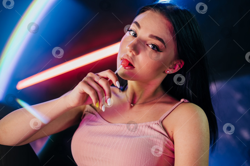 Скачать Чувственные женские красные губы с леденцом на палочке. Концепция моноблока на неоновых огнях. Портрет красивой женщины фотосток Ozero