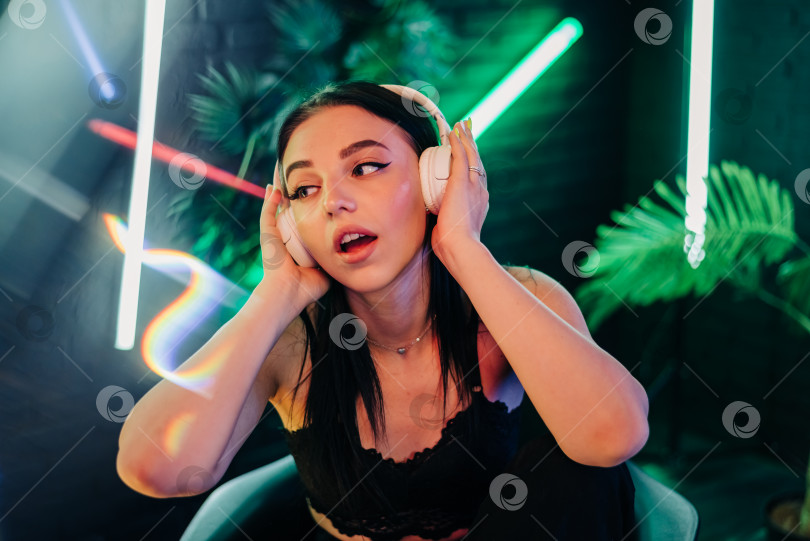 Скачать Модная симпатичная женщина в наушниках слушает музыку на неоновом фоне в студии. фотосток Ozero