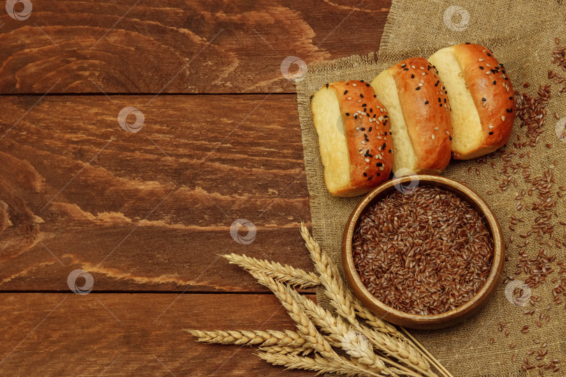 Скачать на льняной салфетке лежат маленькие булочки, посыпанные кунжутом, пучок пшеничных колосьев и миска с семенами льна фотосток Ozero