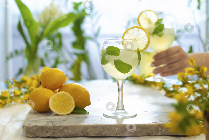 Скачать Цитрусовый лимонад со льдом в кувшине и бокалах с лимонами, украшенный ломтиками лимона, и на мраморном столе в руке с коктейлем фотосток Ozero