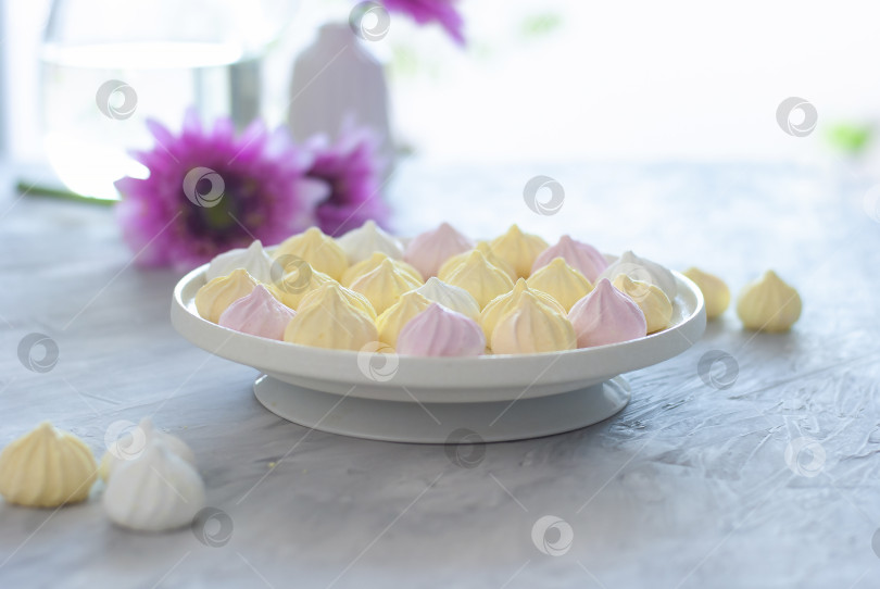 Скачать Мини-меренги розового, белого и желтого цветов в белой миске на белом светло-сером столе. Вкусный десерт крупным планом фотосток Ozero