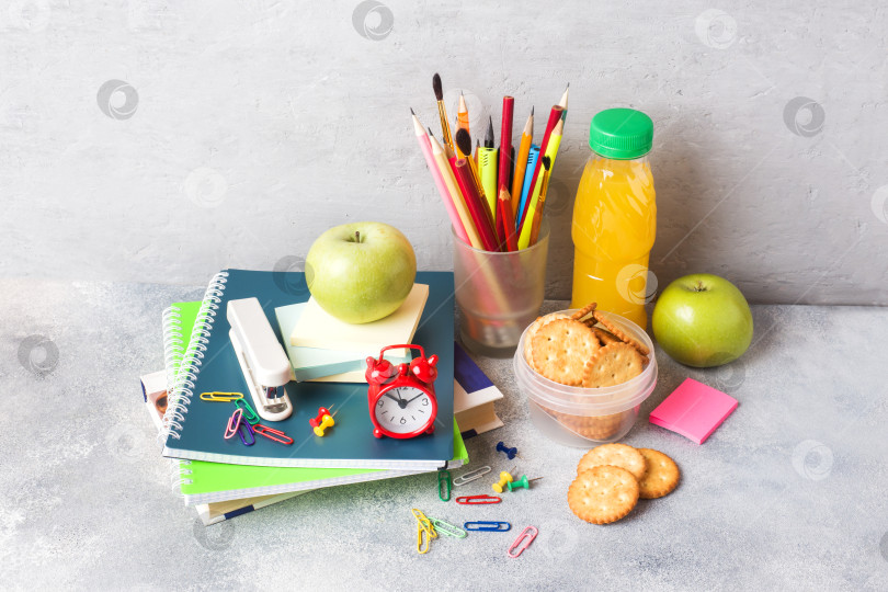 Скачать Школьные принадлежности и крекеры для завтрака, апельсиновый сок и свежее яблоко на сером столе с местом для копирования. концептуальная школа. фотосток Ozero