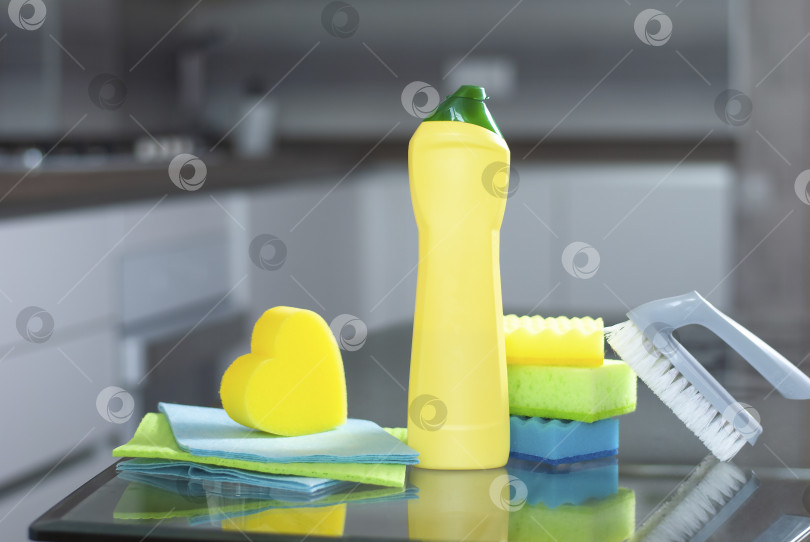 Скачать Ведро с чистящими средствами на стеклянном столе и фоне современной кухни. Набор для стирки разноцветный желтого, зеленого, серого цветов фотосток Ozero