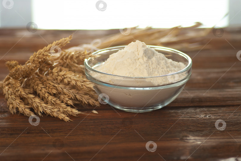Скачать Стеклянная миска с мукой и веточками натуральной пшеницы на темно-коричневом деревянном столе фотосток Ozero