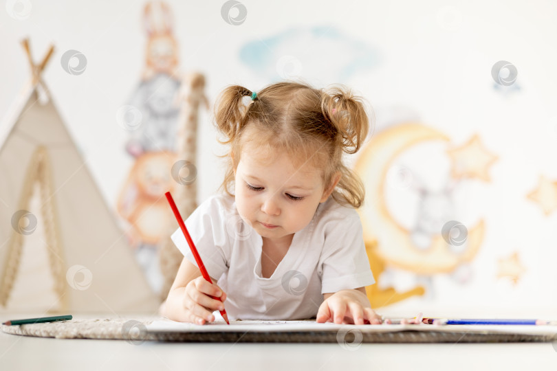 Скачать маленькая девочка-блондинка рисует цветными карандашами на полу в детской комнате, досуг детей, детский сад фотосток Ozero
