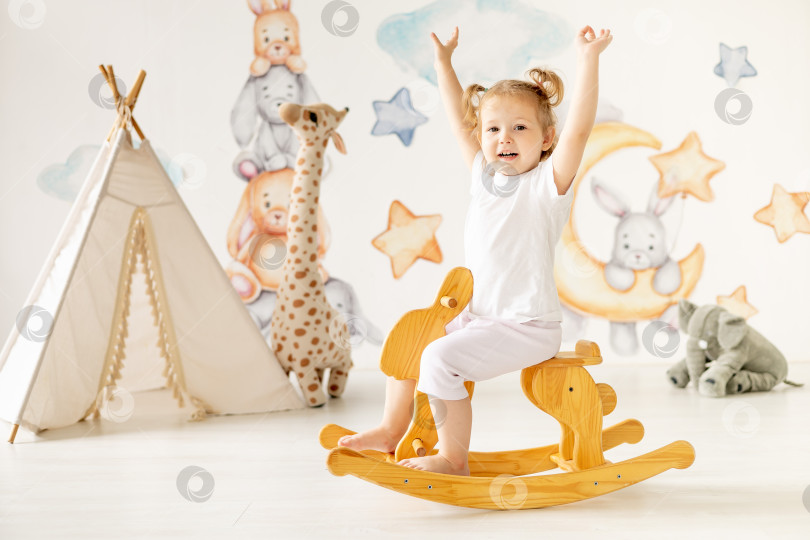 Скачать маленькая девочка-блондинка играет в детской комнате, качаясь на деревянной лошадке, детский досуг, детский сад фотосток Ozero
