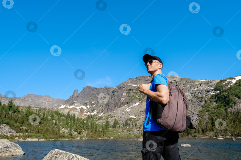 Скачать Турист, стоящий на природе и любующийся живописными пейзажами гор и озера под облачным небом при дневном свете фотосток Ozero