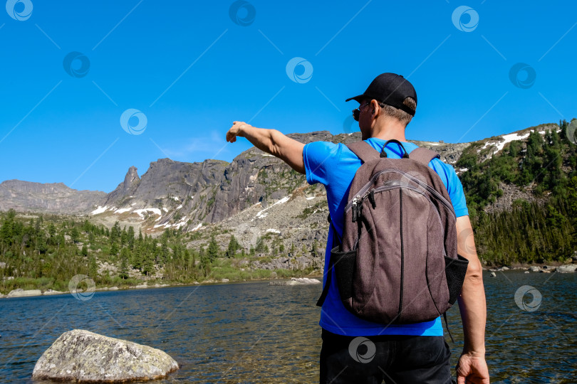 Скачать Турист, стоящий на природе и любующийся живописными пейзажами гор и озера под облачным небом при дневном свете фотосток Ozero