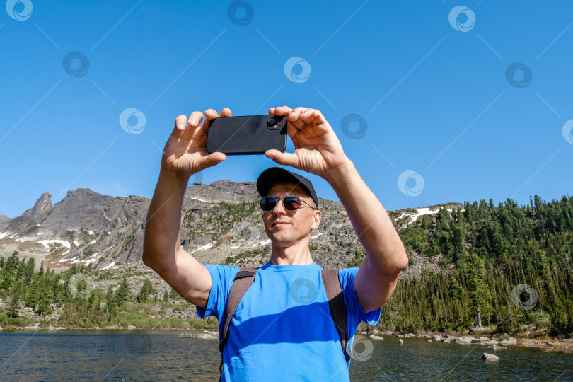 Скачать Путешествующий мужчина использует телефон, чтобы сфотографироваться в горном пейзаже фотосток Ozero