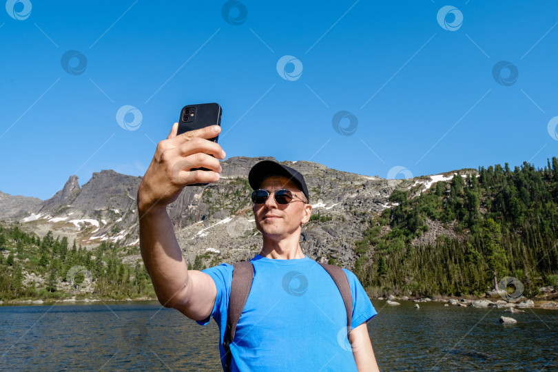 Скачать Путешествующий мужчина использует телефон, чтобы сфотографироваться в горном пейзаже фотосток Ozero