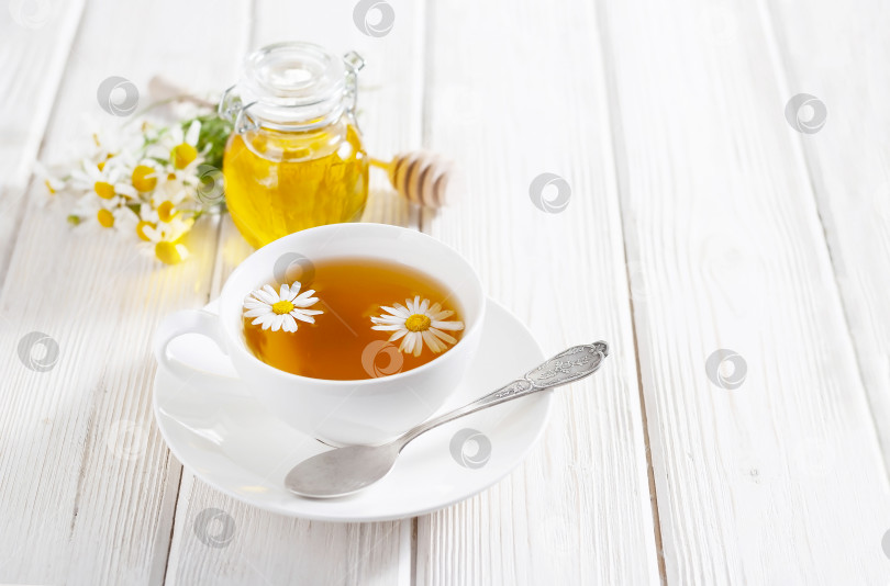 Скачать Белая чашка травяного чая с цветами ромашки и медом на белом деревянном фоне. Натуральная альтернативная медицина фотосток Ozero