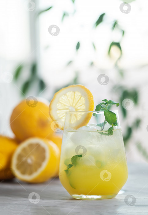 Скачать Освежающий лимонад со льдом в бокале с ломтиком лимона и листьями мяты с лимонными плодами фотосток Ozero