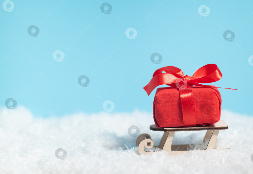 Скачать Деревянные сани, доставляющие красную коробку с подарками на Рождество или Новый год на синем заснеженном фоне фотосток Ozero
