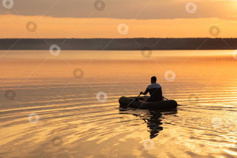 Скачать Мужчина плывет по озеру на надувной лодке на закате фотосток Ozero