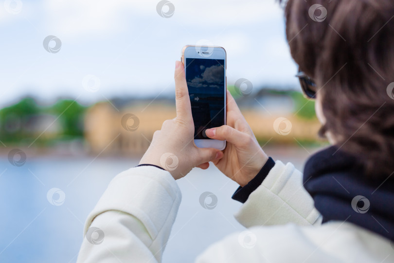 Скачать Молодая женщина на отдыхе использует мобильный телефон, чтобы сфотографировать реку и город фотосток Ozero