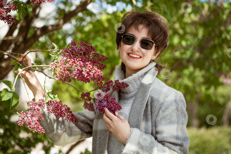 Скачать Портрет молодой женщины в солнцезащитных очках возле куста сирени фотосток Ozero