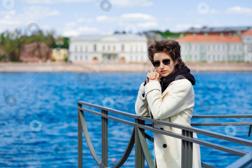 Скачать Красивая молодая женщина прогуливается по набережной в белом пальто и черной толстовке фотосток Ozero