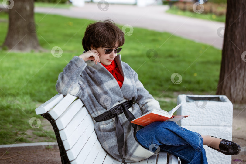 Скачать молодая женщина в парке читает книгу, сидя на скамейке фотосток Ozero