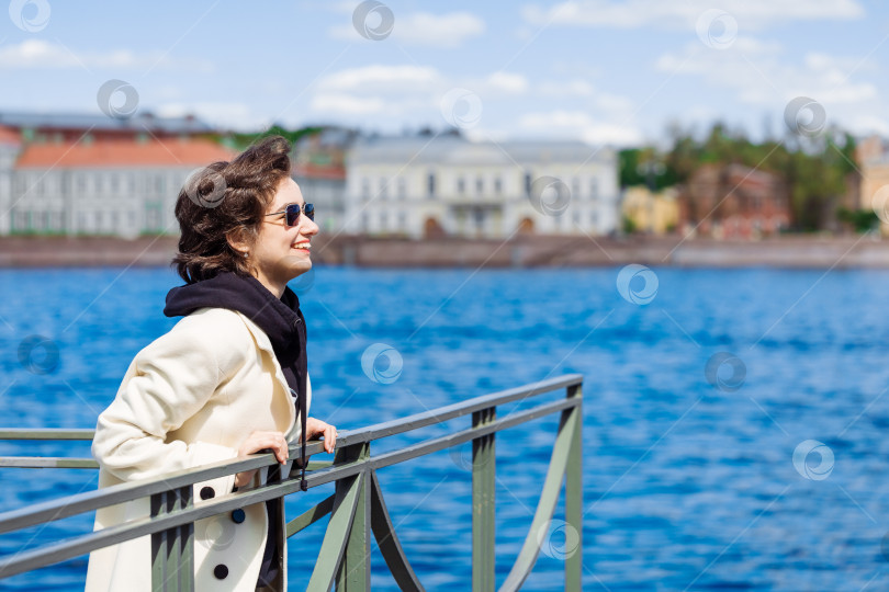 Скачать Счастливая красивая молодая женщина в белом халате и солнцезащитных очках стоит на набережной фотосток Ozero