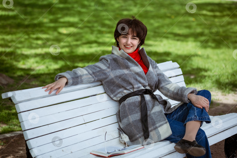 Скачать Счастливая молодая женщина сидит на скамейке в парке фотосток Ozero