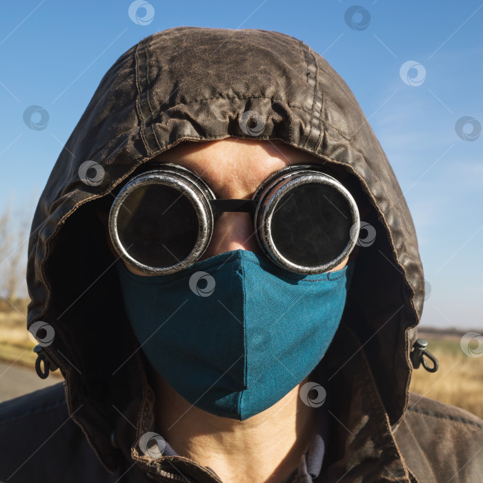 Скачать Мужчина в капюшоне, в винтажных очках в стиле стимпанк и защитной маске от коронавируса, смотрит в камеру крупным планом фотосток Ozero