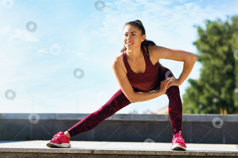 Скачать Красивая девушка-спортсменка выполняет упражнение на растяжку солнечным летним утром на открытом воздухе. Концепция здорового образа жизни и спорта фотосток Ozero