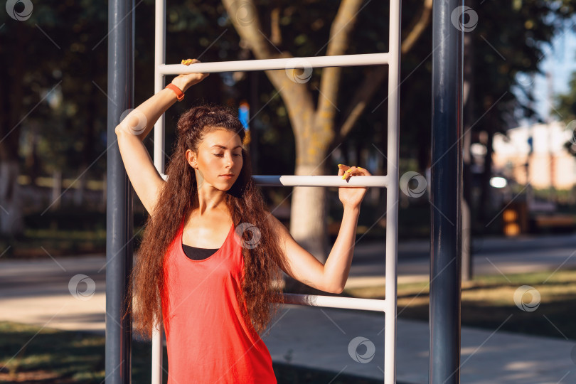Скачать Красивая девушка атлетического телосложения позирует солнечным летним утром возле лестницы на спортивной площадке фотосток Ozero