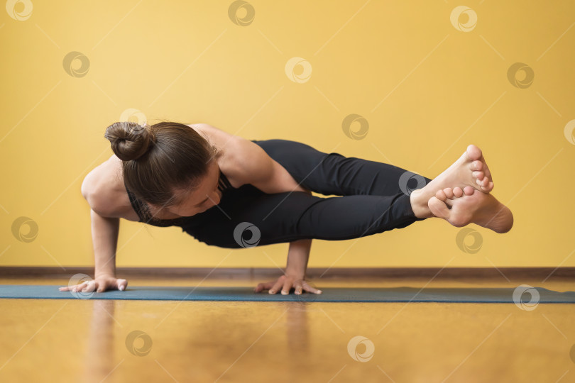 Скачать Женщина в цельном черном спортивном костюме выполняет упражнение Аштавакрасана - стойка на руках на фоне стены фотосток Ozero