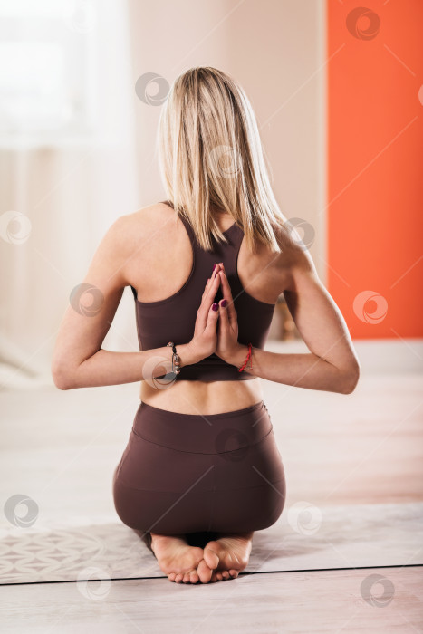 Скачать Блондинка, практикующая йогу, выполняет упражнение Пашчима Намаскарасана, Намасте за спиной. Тренер в спортивной одежде работает дома, чтобы исправить осанку и развить гибкость в верхней части тела фотосток Ozero