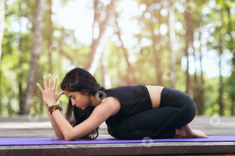 Скачать Женщина-тренер летним солнечным утром в спортивной одежде, сидящая на ковре, практикующая асану йоги, выполняющая позу матери фотосток Ozero