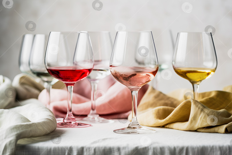 Скачать Разные сорта вина в бокалах на столе с текстильными скатертями на нейтральном сером фоне фотосток Ozero