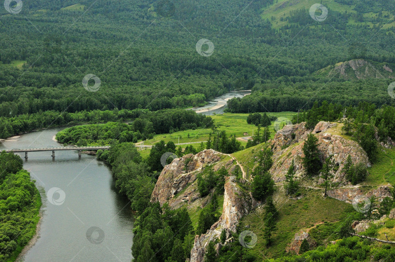 Скачать Вид с вершины горы на русло реки, протекающей через лес, и мост, пересекающий его. фотосток Ozero